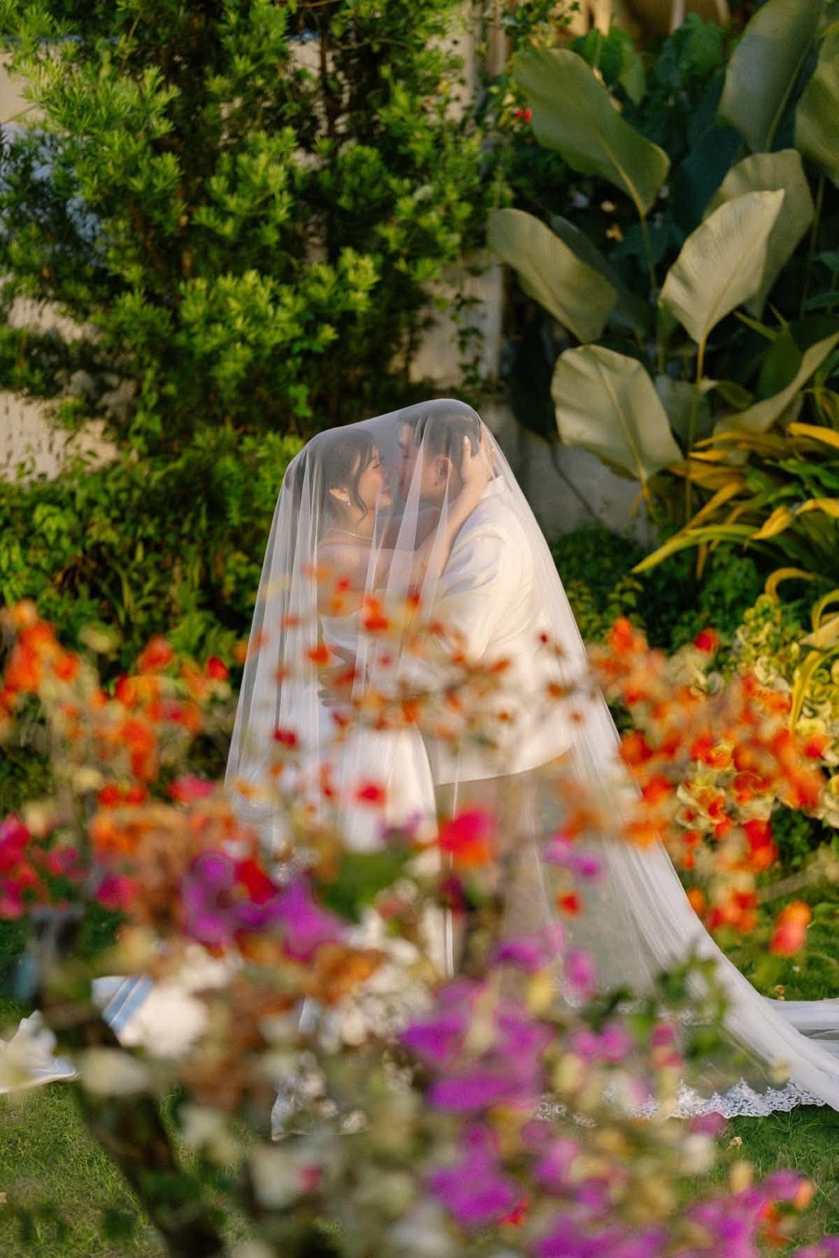 A couple beneath a veil in Casa's flowering garden, in late afternoon light